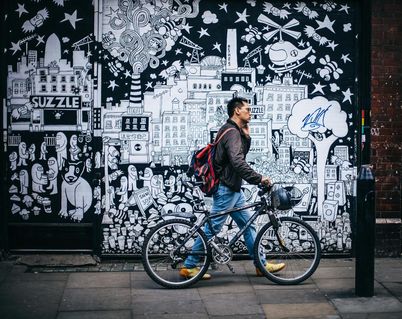 why-choose-us Man walking a bicycle past a detailed urban graffiti mural in a city setting.