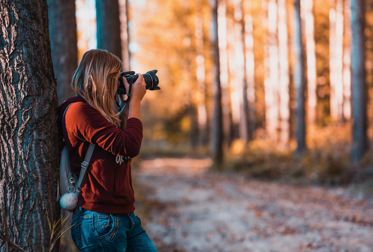 our-story A woman taking photos in an autumn forest, perfectly capturing the beauty of nature.